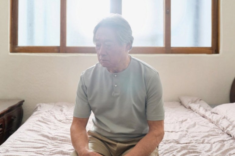 침대에 앉아 기운 없이 고개를 숙인 남성 — 무기력 · 입맛 없음
